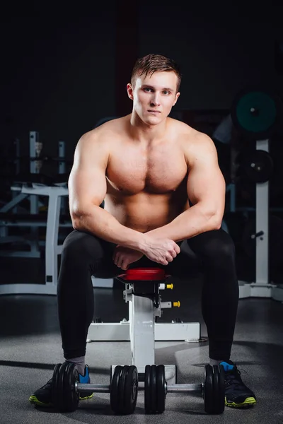 Culturista profesional sentado en el banco, descansando entre ejercicios con pesas en el gimnasio. Grande. —  Fotos de Stock