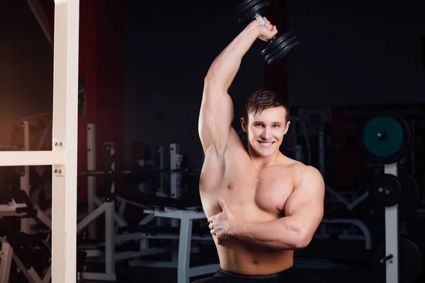 Professionele bodybuilder training met barbell zittend op het bankje op sportschool. Grote zelfverzekerde gespierde man opleiding. — Stockfoto