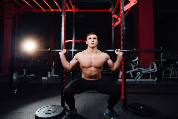 Portrait d'un bel athlète au gymnase. l'homme fait l'exercice avec haltère, debout et accroupi. grand confiant — Photo