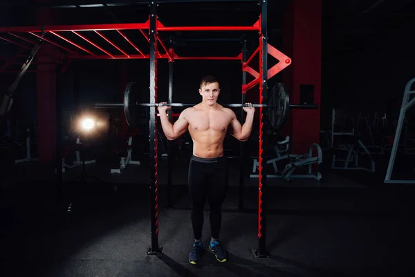 Retrato de un atleta guapo en el gimnasio. hombre hace el ejercicio con la barra, de pie y en cuclillas. gran confianza — Foto de Stock