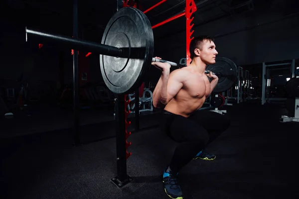 Retrato de um belo atleta no ginásio. homem faz o exercício com barbell, de pé e agachamento. grande confiante — Fotografia de Stock