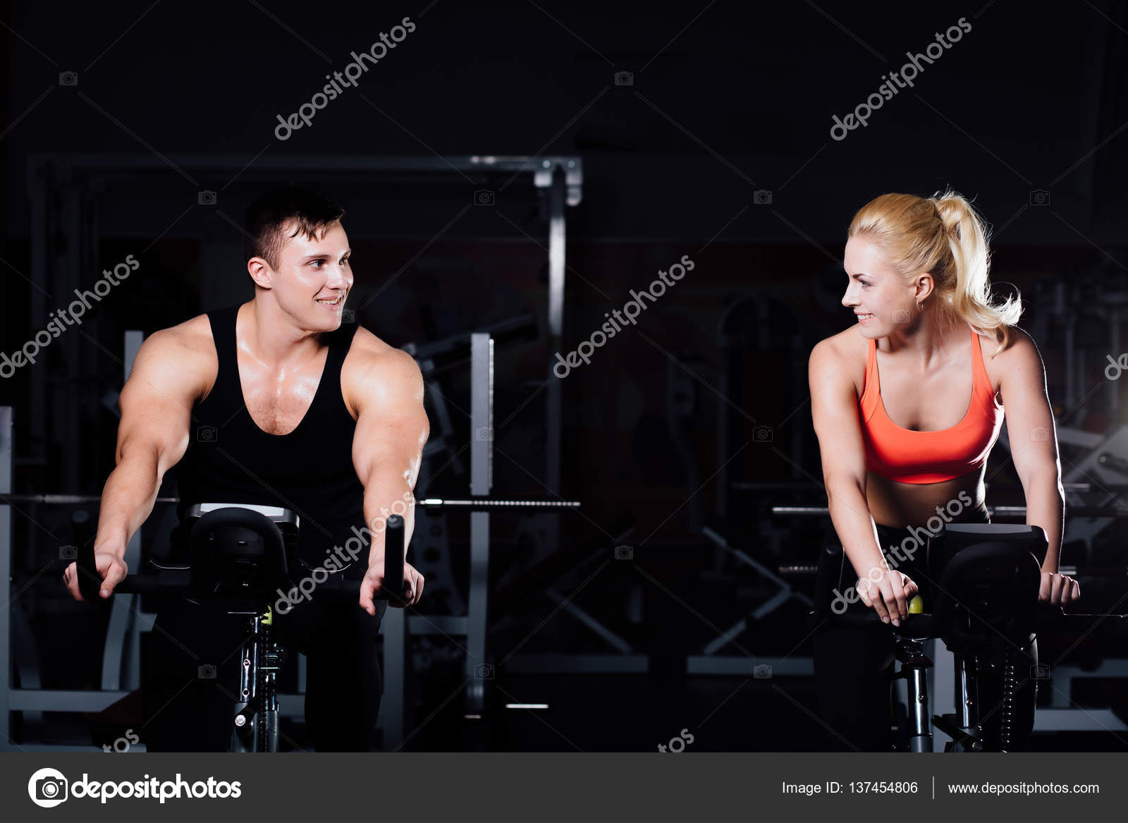 Sporty couple exercising at the fitness the exercise bike on a dark gym.  Stock Photo by ©photominus 137454806