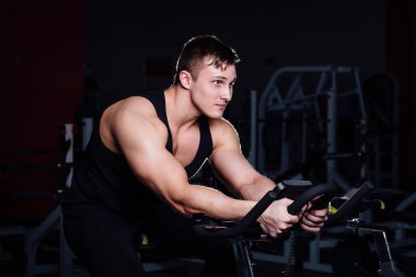 Yakışıklı adam egzersiz fitness egzersiz bisikleti spor salonunda karanlık tarih portresi.