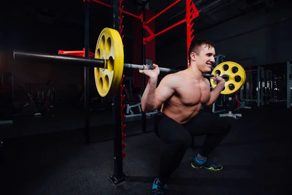 Retrato de un atleta guapo en el gimnasio. hombre hace el ejercicio con la barra, de pie y en cuclillas. gran confianza — Foto de Stock