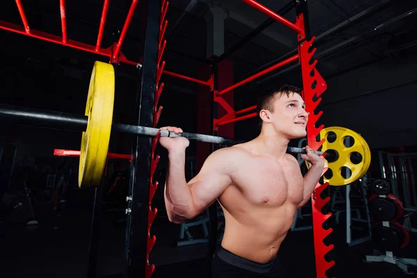 Retrato de un atleta guapo en el gimnasio. hombre hace el ejercicio con la barra, de pie y en cuclillas. gran confianza — Foto de Stock