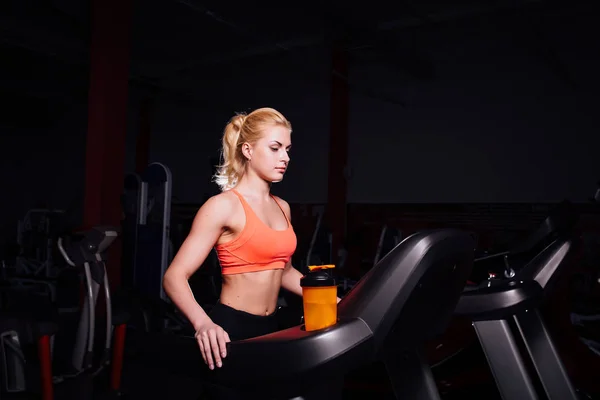 Jovem linda menina bonito no modelo de fitness no ginásio correndo na esteira com garrafa — Fotografia de Stock