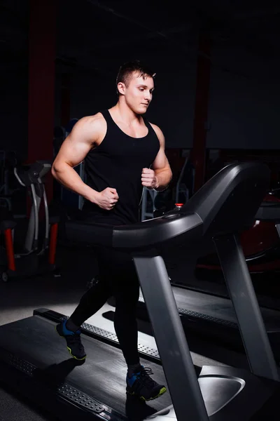 Young strong big man fitness model in the gym running on the treadmill with water bottle.