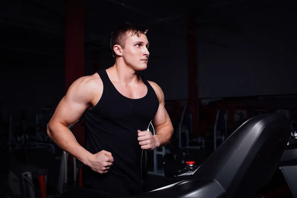 Jeune homme fort grand modèle de remise en forme dans la salle de gym en cours d'exécution sur le tapis roulant avec bouteille d'eau . — Photo