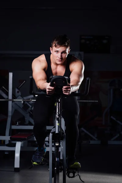 Portret przystojny mężczyzna treningu na fitness rower treningowy ciemny siłowni. — Zdjęcie stockowe