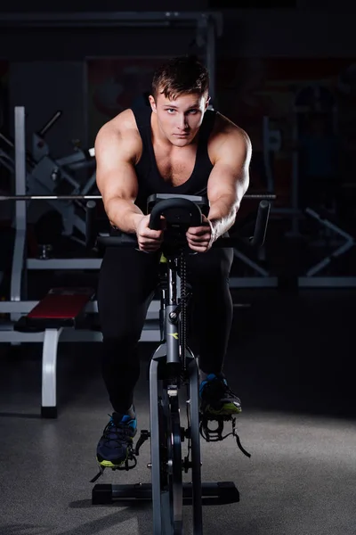 Portret przystojny mężczyzna treningu na fitness rower treningowy ciemny siłowni. — Zdjęcie stockowe
