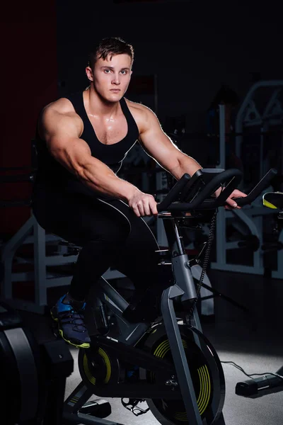Retrato de un hombre guapo entrenar en fitness la bicicleta de ejercicio oscuro en el gimnasio . —  Fotos de Stock