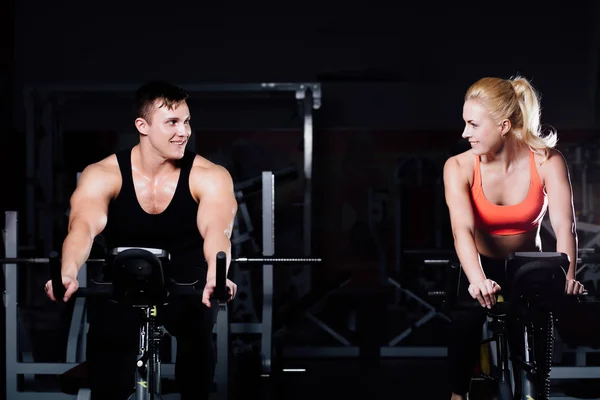 在健身锻炼运动自行车上黑暗的健身房运动夫妇. — 图库照片