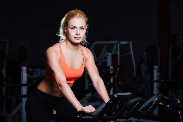 Retrato de un lindo entrenamiento femenino agradable en fitness la bicicleta de ejercicio oscura en el gimnasio . —  Fotos de Stock