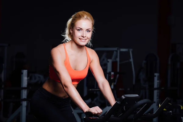 Retrato de un lindo entrenamiento femenino agradable en fitness la bicicleta de ejercicio oscura en el gimnasio . —  Fotos de Stock