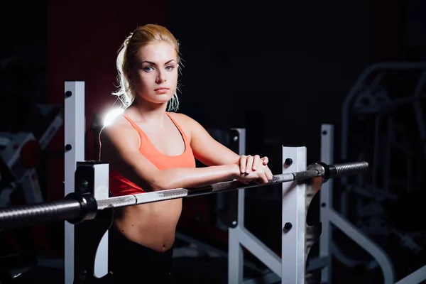Blondes Fitness-Girl mit perfekter Figur ruht sich nach dem Sport-Training im Fitnessstudio an die Langhantel gelehnt aus — Stockfoto