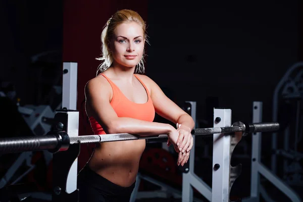 Chica rubia fitness con forma perfecta cuerpo descansa después del entrenamiento deportivo en el gimnasio apoyado en la barra —  Fotos de Stock