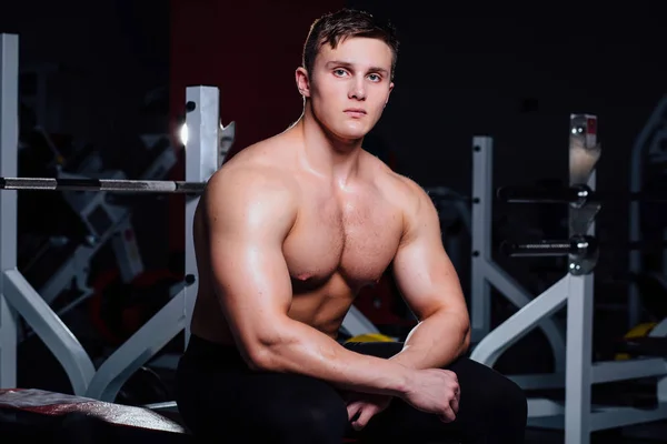 Joven hombre guapo relajándose en el banco de pesas después del entrenamiento en el gimnasio —  Fotos de Stock