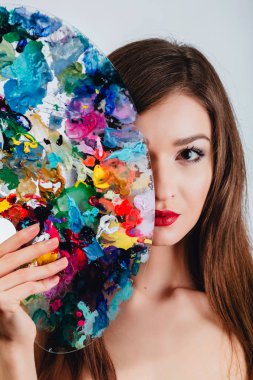 Çıplak çekici genç kadın sanatçı bir renk paleti ve fırça, kameraya bakıyor tutuyor. Stüdyo beyaz arka plan.