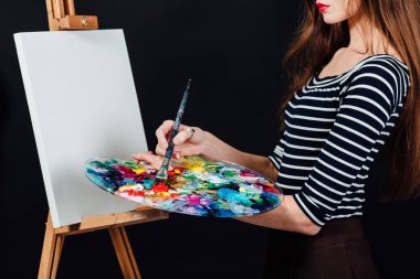 Bir resim tuval üzerine bir şövale resmi sevimli güzel kız ressamın. Metin için yer. Studio siyah arka plan.