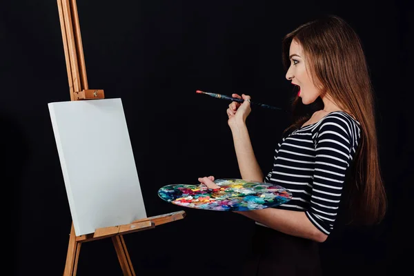 Roztomilá krásná dívka umělec maluje obraz na plátně stojan. Prostor pro text. Studio černé pozadí. — Stock fotografie
