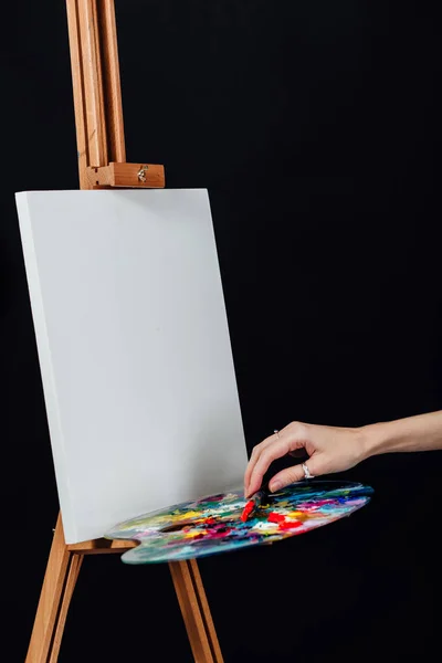 Carino bella ragazza artista pittura un quadro su tela un cavalletto. Spazio per il testo. Studio sfondo nero . — Foto Stock