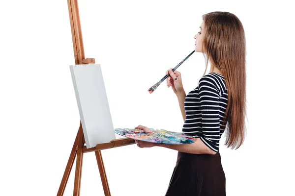 Симпатичная красивая девушка художник рисует картину на холсте мольберта. Пространство для текста. Студия белый фон, изолированный . — стоковое фото