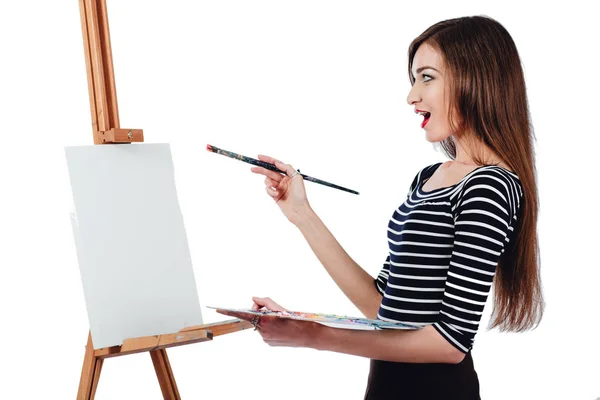 Симпатичная красивая девушка художник рисует картину на холсте мольберта. Пространство для текста. Студия белый фон, изолированный . — стоковое фото