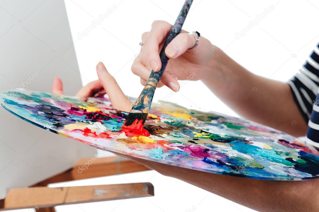 Cute beautiful girl artist painting a picture on  canvas  easel. Space for text. Studio white background, isolated.