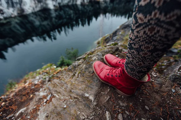 Creative girl standing on the edge of a picturesque cliff. Tourist in jeans and red boots hipster sneakers. — Stock Photo, Image