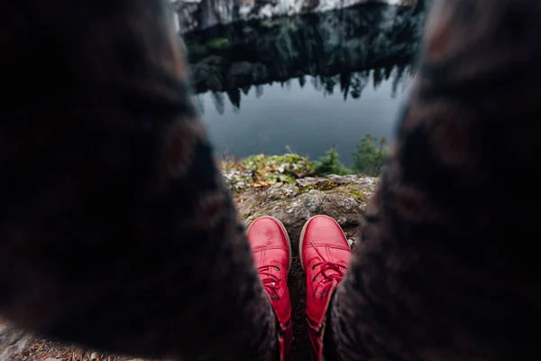 Creative girl standing on the edge of a picturesque cliff. Tourist in jeans and red boots hipster sneakers. — Stock Photo, Image