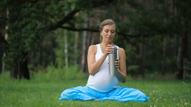 Těhotné Jóga v lotosové pozici s termosky čaj. v parku na trávě, venkovní, zdraví ženy, Žena. — Stock video