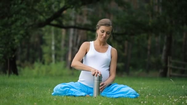 Беременная йога в позе лотоса с термосом, пьющим чай. in the park on the grass, outdoor, health woman, female . — стоковое видео