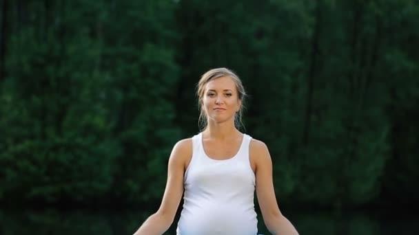 Junge Frau in Lotusposition praktiziert Yoga im Wald neben dem Fluss. auf Matten sitzend den hölzernen Steg. — Stockvideo