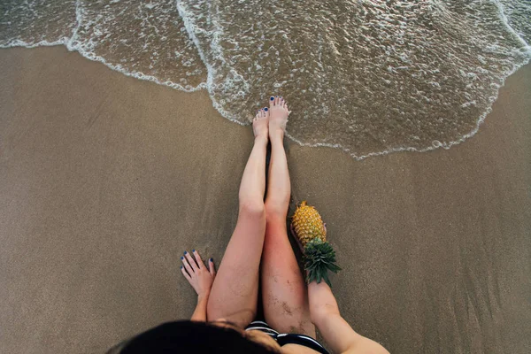 在海滩上，一个菠萝，手中的美丽长女性腿顶视图. — 图库照片