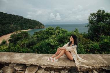 Bir arka plan bir deniz kıyısında Körfezi harap bir binanın çatısında bir genç turist kız oturuyor.