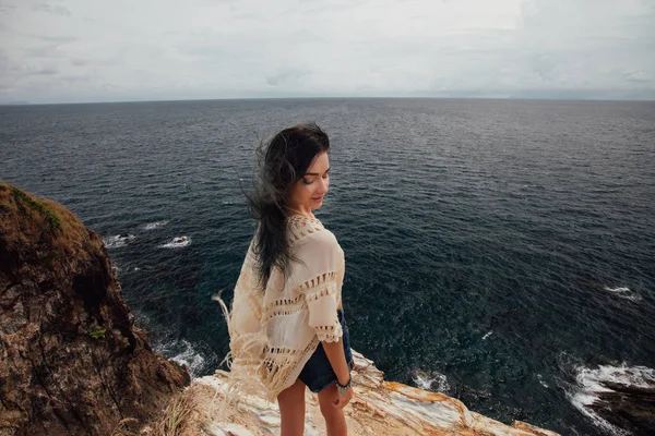 Νεαρή γυναίκα στέκεται στην άκρη των βράχων και να ψάχνει σε μια μεγάλη θάλασσα. — Φωτογραφία Αρχείου