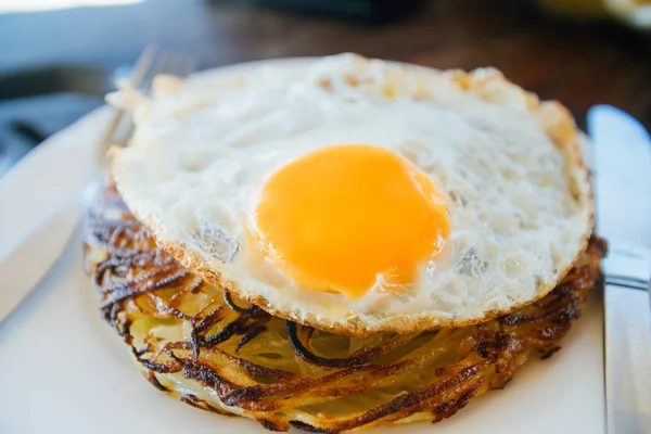 Panquecas de batata com ovos fritos são servidas com uma faca e garfo. Na mesa de carvalho. Café à beira-mar . — Fotografia de Stock