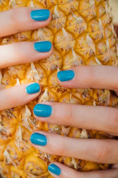 Girl with a turquoise manicure holds a ripe pineapple in her hands. — Stock Photo, Image