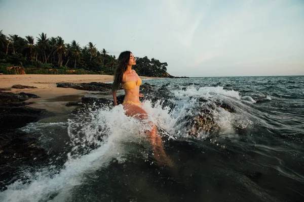 Sensual jovem morena beleza vestindo maiô amarelo com cabelo bonito sentado em pedra na praia — Fotografia de Stock