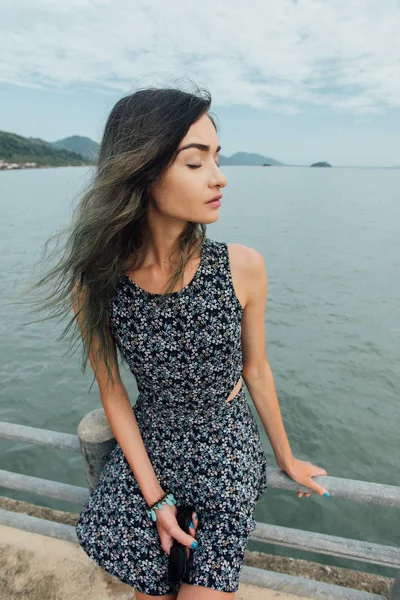 Young beautiful woman in dress sitting on the pier and relaxing with blue sky and sea background — Stock Photo, Image