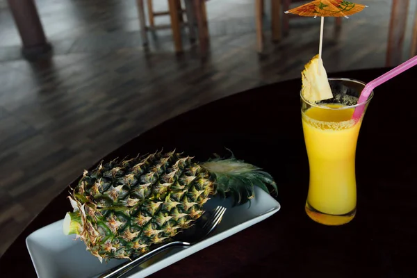 Fried rice inside pineapple next to a glass of juice with a straw and slices of fruit.