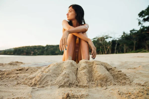 年轻漂亮的女人埋在海滩上的沙子的双腿。性感的女人坐在沙滩上 — 图库照片