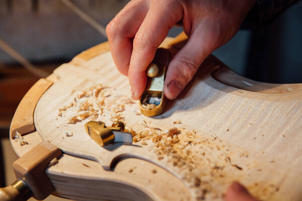 Master artisan luthier working on the creation of a violin. painstaking detailed work on wood.