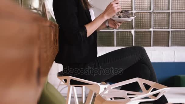 Mulher de negócios jovem bonita comendo um bolo com uma colher em um café em um fundo de balcão de bar . — Vídeo de Stock