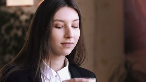 Mladá žena pít cappuccino nebo čaj s mlékem a usmívá se na kameru. — Stock video