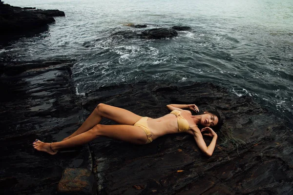 Sexy jovem encontra-se em uma costa do oceano de rocha. Menina bonita no fundo pedregoso — Fotografia de Stock