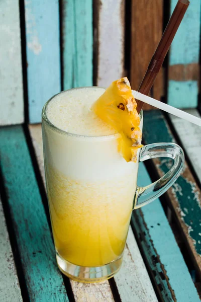 Gult glas cocktail med en bit ananas på färgglada träskiva bakgrund — Stockfoto