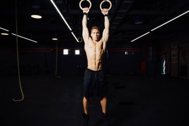 Genç formda adam jimnastik yüzüklerini çekiyor..