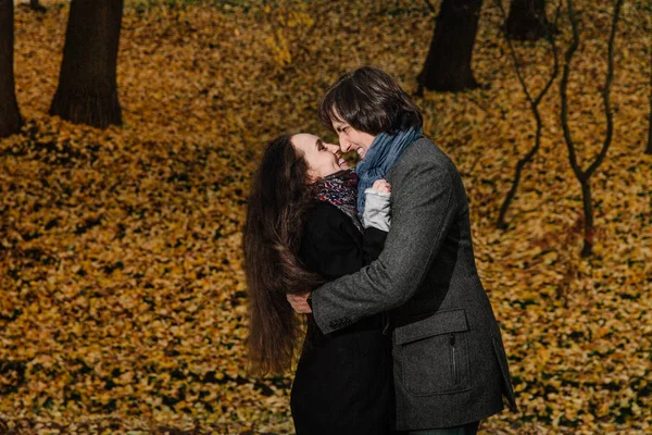 Abraços de casal em um parque de queda. Outono dourado no fundo com folhas e árvores, folhagem . — Fotografia de Stock