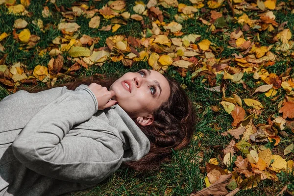 秋天的女孩躺在森林公园的草坪上的画像。长长的头发枯黄的落叶上. — 图库照片